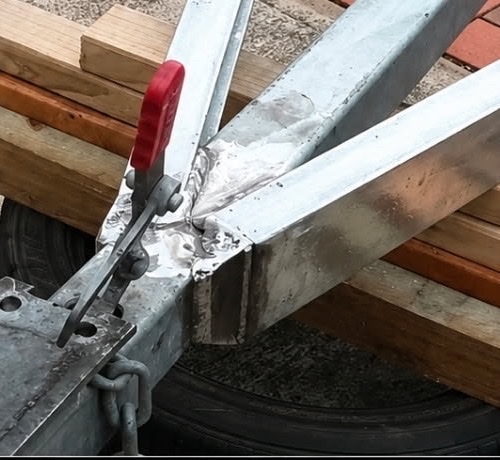 Close-up of a built-up weld joining the galvanised trailer brace, clamped in position
